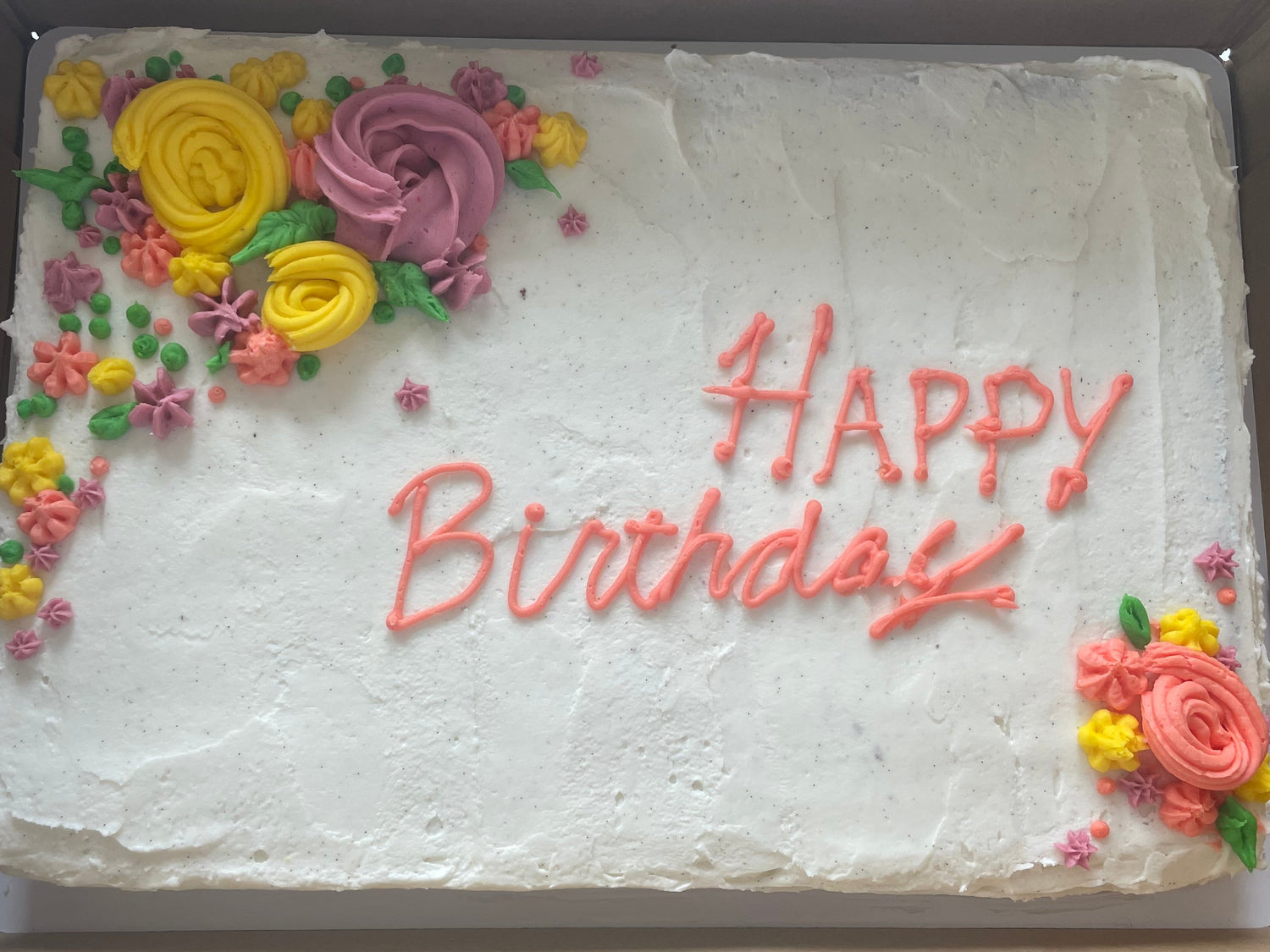 Birthday cake with white frosting, colorful flowers, and 'Happy Birthday' text in a cardboard box.